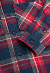 Koszula z flaneli w kratę w kolorach czerwonym i granatowym, z zapinanym na guziki przodem, kieszenią na piersi oraz fakturą tkaniny z poziomymi i pionowymi paskami.