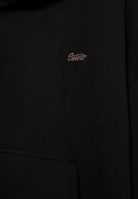 Black sweatshirt with a small gray embroidered text logo "SWTZ" on the left chest and a front pocket at the bottom.