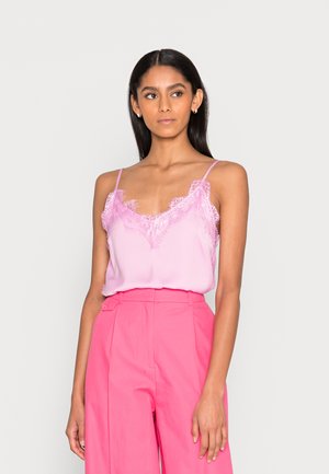 Camisola de cetim rosa com acabamento de renda, apresentando alças finas e um corte solto, combinada com calças rosa de cintura alta.