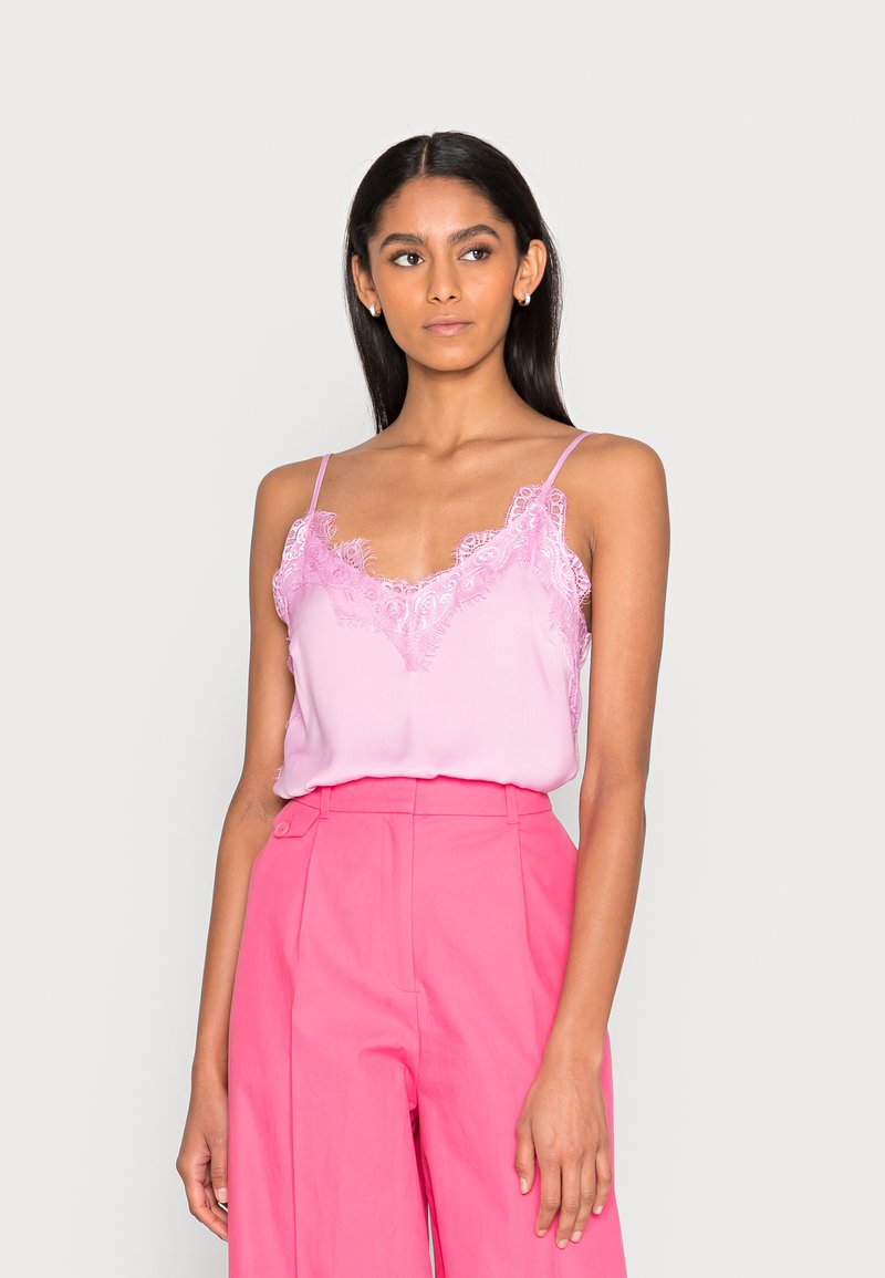 Camisola de cetim rosa com acabamento de renda, apresentando alças finas e um corte solto, combinada com calças rosa de cintura alta.
