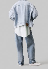 Ljusblå denimoversizejacka med rå kant, kombinerad med en vit skjorta med krage och baggy ljusdenimjeans. Vita sneakers fulländar looken.