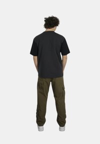 T-shirt nera a maniche corte, vestibilità comoda, abbinata a pantaloni cargo oliva con ampie tasche laterali e sneakers bianche. Vista posteriore mostrata.