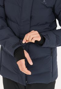 Marineblau isolierte Jacke mit puffigem Design; verfügt über einen Klettverschluss an den Bündchen, eine glatte Textur und eine schlanke Silhouette; Reißverschlüsse an den Taschen sind sichtbar.