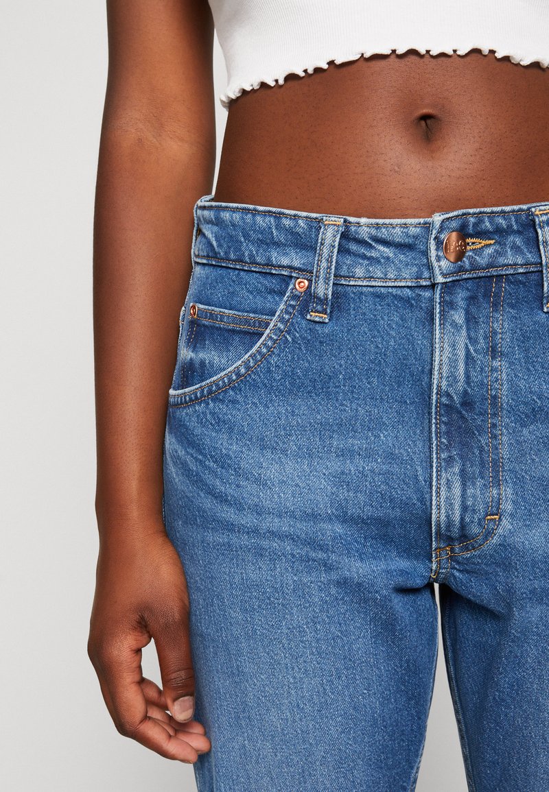 Hochgeschnittene blaue Denim-Jeans mit kupferfarbenen Beschlägen, Kontrastnähten und klassischem Fünf-Taschen-Design. Weiche Textur mit einem verblassten Finish.