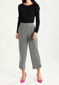 Pull noir à manches longues associé à un pantalon large gris à motifs et des escarpins roses ; comprend un haut cintré et des plis sur le pantalon.