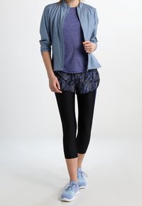 Ljusblå idrottsjacka, lila topp, mönstrade svarta shorts, svarta capri leggings och ljusblå skor. Släta texturer och figurnära design.