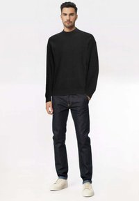 Maglione nero a maniche lunghe, jeans scuri e sneakers bianche. Il maglione presenta un collo semplice; i jeans hanno una vestibilità slim e cuciture sottili.