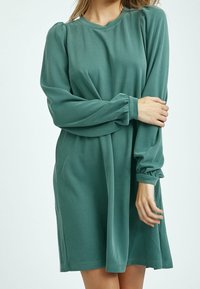 Dlouhá, volně padnoucí šaty z měkké, tyrkysové látky. Mají nařasené rukávy a kulatý výstřih. Jednoduchý, nezdobený design.