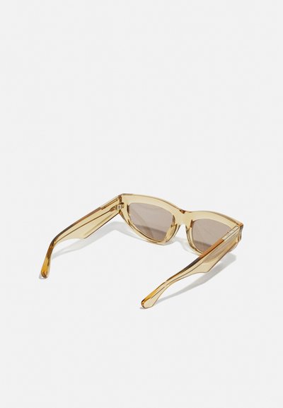 Yellow-tinted sunglasses with a geometric design, transparent frame, and brown tinted lenses. Thin arms with angled tips.