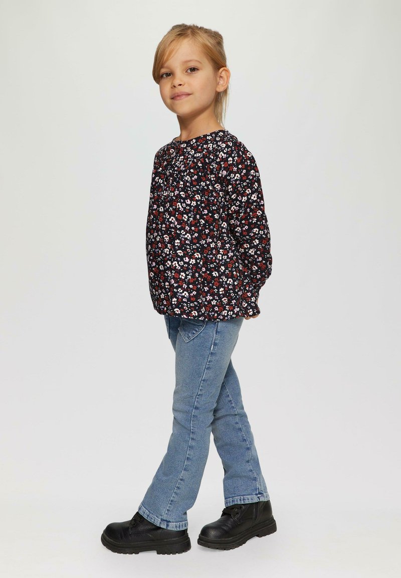 Langarm bloes met een zwarte achtergrond en rode en witte bloemen, gecombineerd met lichtblauwe jeans en zwarte laarzen.