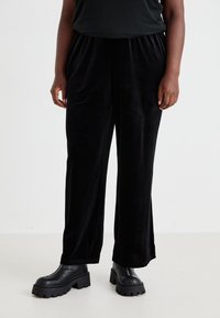 Pantalones de terciopelo negro de pierna ancha con cintura elástica, que presentan una textura suave y un ajuste relajado, combinados con botines negros de plataforma.