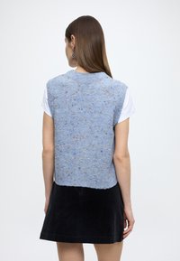 Mouwloos blauw gebreid topje met gespikkelde patronen, voorzien van een ronde halslijn en gestructureerde stof, gecombineerd met een zwarte rok.