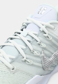 Light blue athletic shoe featuring textured fabric, metallic accents, and white laces. Notable silver Nike swoosh on the side.