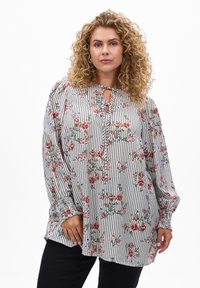 Blouse à motif floral avec des rayures verticales noires et blanches. Présente un col en forme de clé et des manches longues à volants. Tissu texturé.