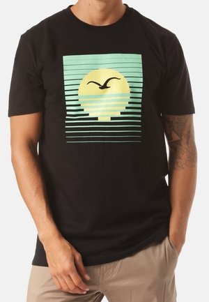 Schwarzes Baumwoll-T-Shirt mit einem aufgedruckten Design bestehend aus einem gelben Kreis und türkisfarbenen Streifen, das eine Vogelsilhouette über dem Kreis zeigt.