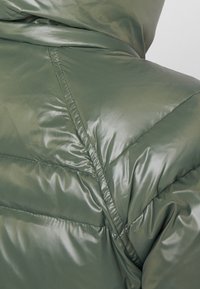 Olivgrüne Steppjacke mit glänzendem Finish, mit gesteppten Bereichen und Kapuze. Der Stoff wirkt glatt und isoliert.