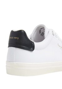 Sneaker bianca con dettaglio del tallone in pelle nera, caratterizzata dalla scritta "SINCE 1973" in rilievo dorato. Tessuto testurizzato e suola in gomma bianca.