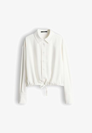 Camicia bianca a manica lunga con chiusura frontale con bottoni, collo ampio, vita elasticizzata e coulisse, realizzata in un tessuto liscio e leggero.