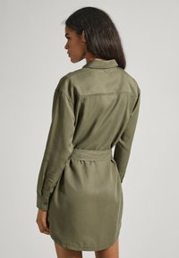 Abito camicia verde oliva, maniche lunghe, vita cintrata, texture morbida del tessuto, giromanica singolo al retro e polsini con bottoni.