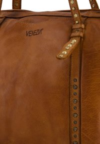 Tan leather handbag featuring metal studs along the strap, embossed "VENEZIA" logo, and a textured surface.