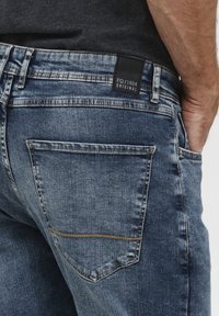 Jeans in denim con un lavaggio blu sbiadito e un taglio dritto. Presentano un'etichetta nera del marchio sulla vita e una tasca posteriore cucita singolarmente.