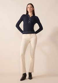 Polo long à manches longues côtelé marine avec une patte de boutonnage et trois boutons, associé à un pantalon droit crème et des bottes à talons noires.
