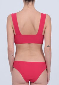 Ensemble de bikini fuchsia comprenant un haut bralette à larges bretelles et un bas assorti. Texture lisse, design minimaliste.