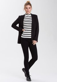 Czarna marynarka na czarnym i białym paskowanym golfie, zestawiona z czarnymi leginsami i czarnymi butami na sznurówki. Minimalistyczny design i dopasowany krój.