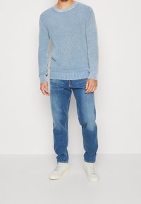 Jasnoniebieski sweter z dzianiny o prążkowanej fakturze, z okrągłym dekoltem i długimi rękawami, zestawiony z jasnoniebieskimi dżinsami i białymi trampkami.