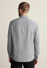 Herrskjorta med lång ärm i rutigt mönster med blå och vita nyanser. Har en krage med knappar och knappar på ärmsluten. Tillverkad av bomull.