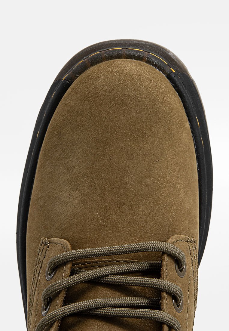 Zapato de ante marrón con puntera redondeada y suela de goma negra. Presenta agujetas grises y un detalle de costura a lo largo del costado.