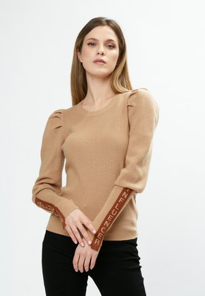 Strickpullover in Hellbraun mit Puffärmeln und kontrastierenden, dunkelbraunen, markierten Bündchen, die das Wort "INFLUENCER" in Fettdruck tragen.