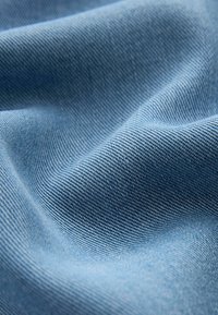 Modrá denimová tkanina s hladkým povrchem a viditelným vzorem tkaní, která ukazuje jemné varianty tónu a hloubky.