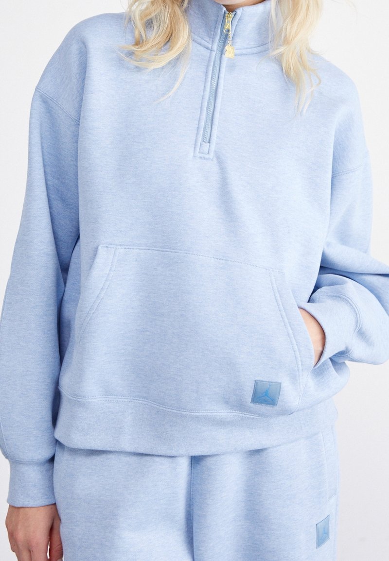 Sudadera de mezcla de algodón de color azul claro, con cuello alto, cierre de media cremallera y bolsillo frontal. Presenta un parche de logotipo texturizado en el dobladillo.