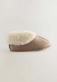 Chaussons en daim marron avec une doublure et un revers en peluche couleur crème. Ils présentent un orteil arrondi et des coutures visibles le long de la semelle.