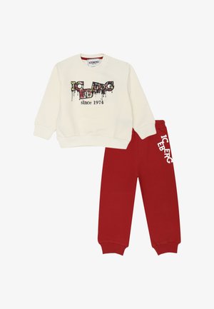 Felpa crema con testo in stile graffiti multicolore "ICEBERG dal 1974" abbinata a pantaloni della tuta rossi con logo bianco "ICEBERG" sulla gamba.