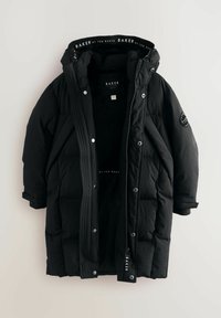 Veste en duvet noire matelassée avec capuche, fermetures à pression et zip. Comprend des accents de logo et des détails côtelés à l'avant. Texture lisse.