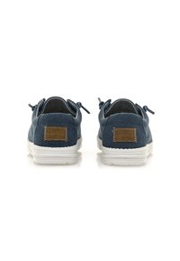 Scarpe da ginnastica blu in tela con suola in gomma bianca, interno a righe e una patch in pelle marrone sul tallone. Punta arrotondata e design con lacci.