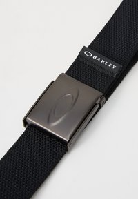 Sort vævet nylonbælte med en mat sort metalspænde. Har et Oakley-maerke syet på remmen.