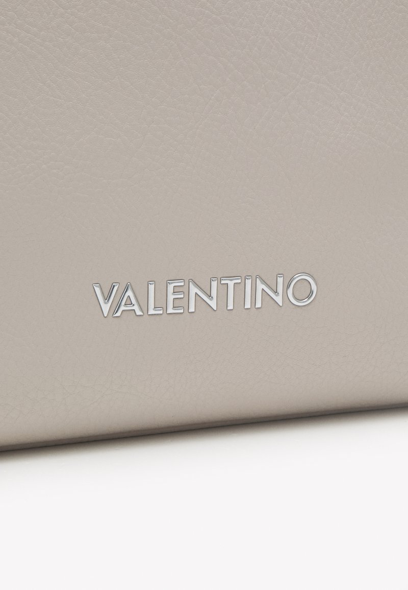 Bolso de cuero beige con un acabado texturizado que presenta la palabra "VALENTINO" en plata, grabada en la parte inferior.