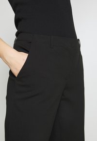 Černé kalhoty vyrobené z hladkého materiálu, s bočními kapsami, rovného střihu a jemnými švy kolem pásu.