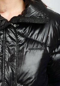 Giacca a vento nera con finitura lucida, dotata di colletto alto, chiusura con zip e logo in rilievo "SEMICOUTURE" frontale.