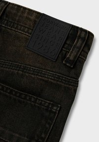 Donkere spijkerbroek van denim met een gestructureerde zwarte leren patch met het etiket "FORWARD JEANS WEAR SINCE 1986." Inclusief details van de achterzak en stiksels.
