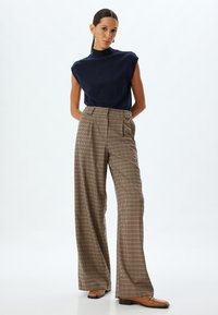 Marineblauw mouwloos topje, hoge hals; brede geruite broek in beige, oranje en groen; bruine loafers. Gladde stof, nauwsluitende pasvorm, casual ontwerp.