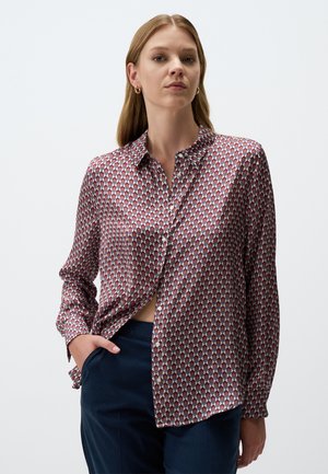 Langärmliges Hemd mit einem rot-blauen geometrischen Muster, aus glattem Stoff gefertigt, mit Kragen und Knopfleiste, in dunkle Hose gesteckt.