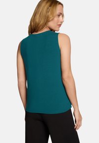 Haut sans manches turquoise avec un col rond et une texture lisse, vu de dos, associé à un bas noir. Design simple et ajusté.