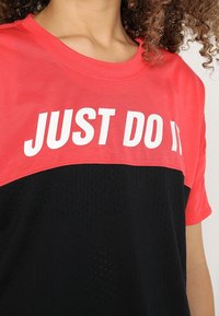 Červené a černé sportovní tričko s krátkým rukávem a síťovanou texturou. Na horní části se nachází bílý tučný nápis "JUST DO IT".