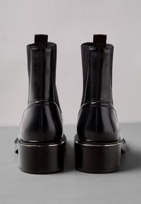 Svarta läderankelstövlar med elastiska sidopaneler, rund tå och tjock klack. Slät textur med en blank yta och kontrasterande sömmar.