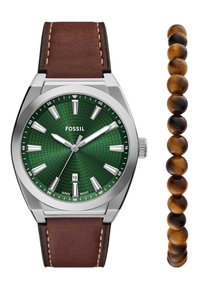 Reloj Fossil con esfera verde estampada, manecillas plateadas y correa de cuero marrón. Incluye una pulsera acompañante de cuentas de ojo de tigre marrón pulidas.