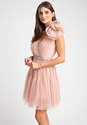 Różowa sukienka z tiulu z głębokim dekoltem w kształcie V, ozdobiona dużym falbaniastym detalem na ramieniu i błyszczącym paskiem w talii. Rozszerzana, warstwowa spódnica.